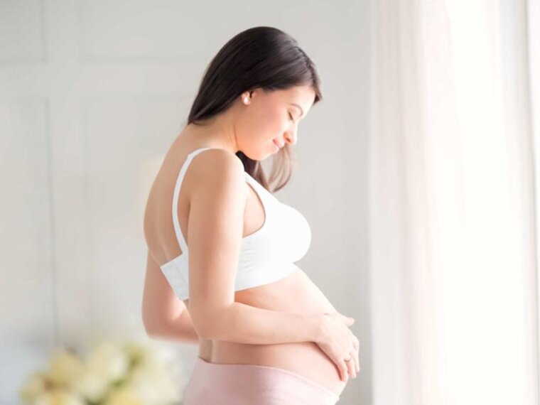 Seitenansicht einer schwangeren Frau, die mit den Händen auf ihrem schwangeren Bauch steht und nach unten schaut.