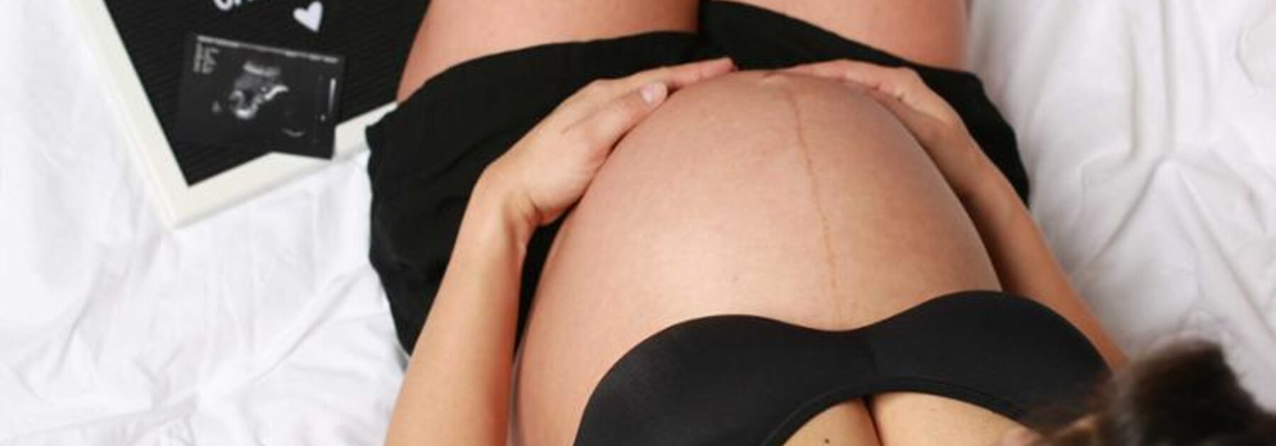 Eine schwangere Frau sitzt auf einem Bett mit einem Ultraschallbild und einer Geburtsanzeige.