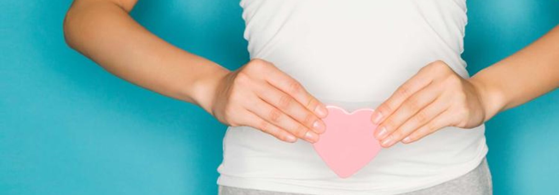 Eine stehende Frau hält sich ein Herz vor den Bauch.