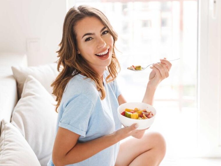 Eine schwangere Frau isst Obst, während sie auf einer Couch sitzt.