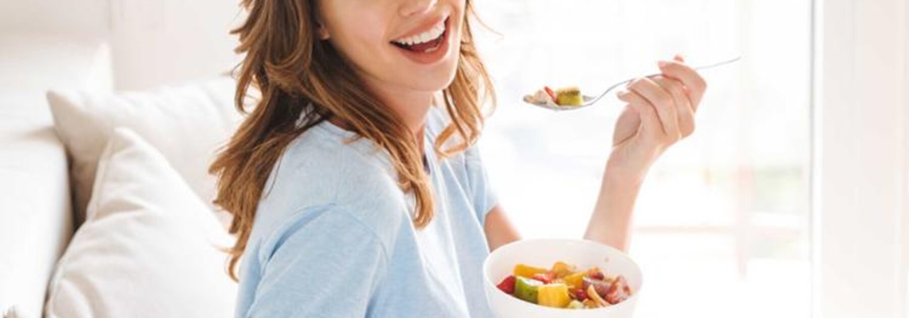 Eine schwangere Frau isst Obst, während sie auf einer Couch sitzt.