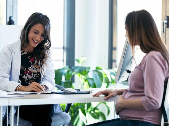 Pregnant woman sitting across the desk from her doctor.