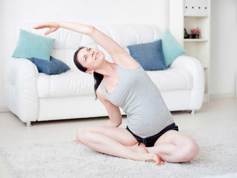 Eine schwangere Frau sitzt zu Hause auf dem Boden und macht Übungen.