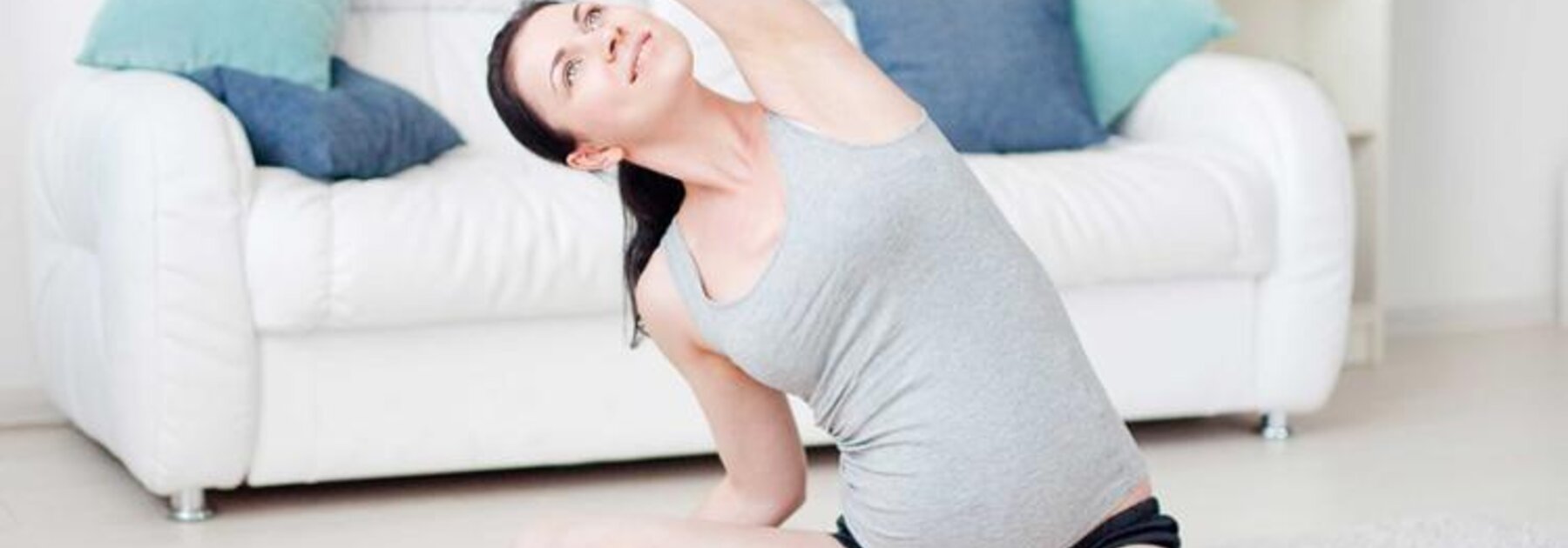 Eine schwangere Frau sitzt zu Hause auf dem Boden und macht Übungen.