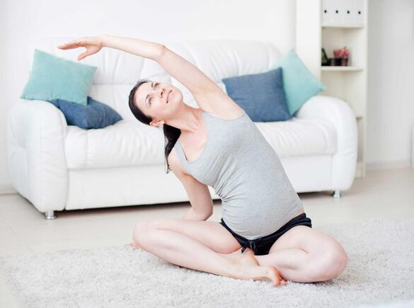 Eine schwangere Frau sitzt zu Hause auf dem Boden und macht Übungen.