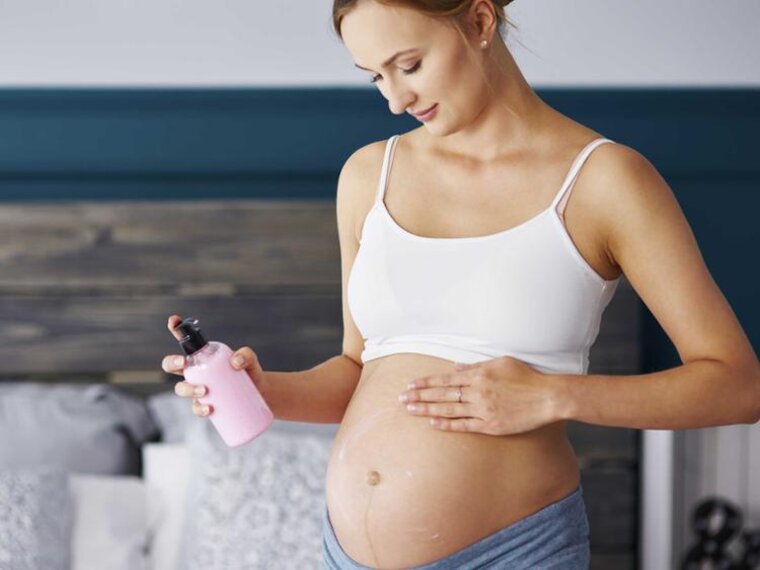 Frau reibt ihren schwangeren Bauch mit Lotion ein.