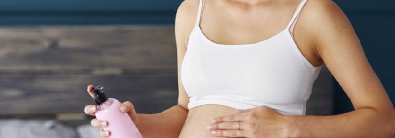 Frau reibt ihren schwangeren Bauch mit Lotion ein.