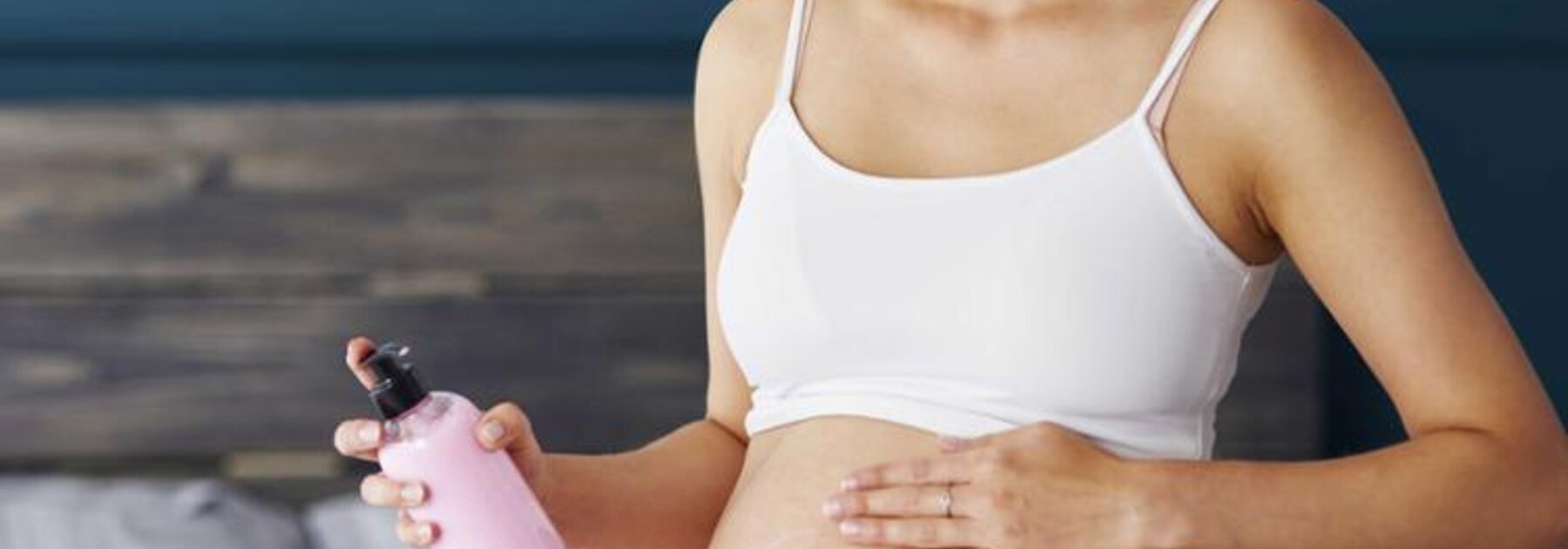 Frau reibt ihren schwangeren Bauch mit Lotion ein.