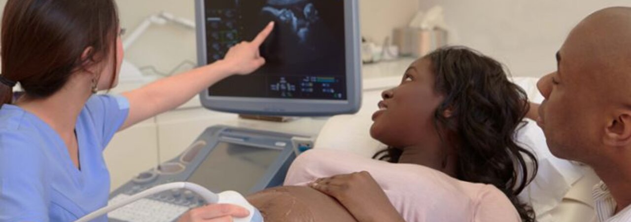 Een zwangere vrouw wordt onderzocht met een echografie terwijl de vader naast haar zit.
