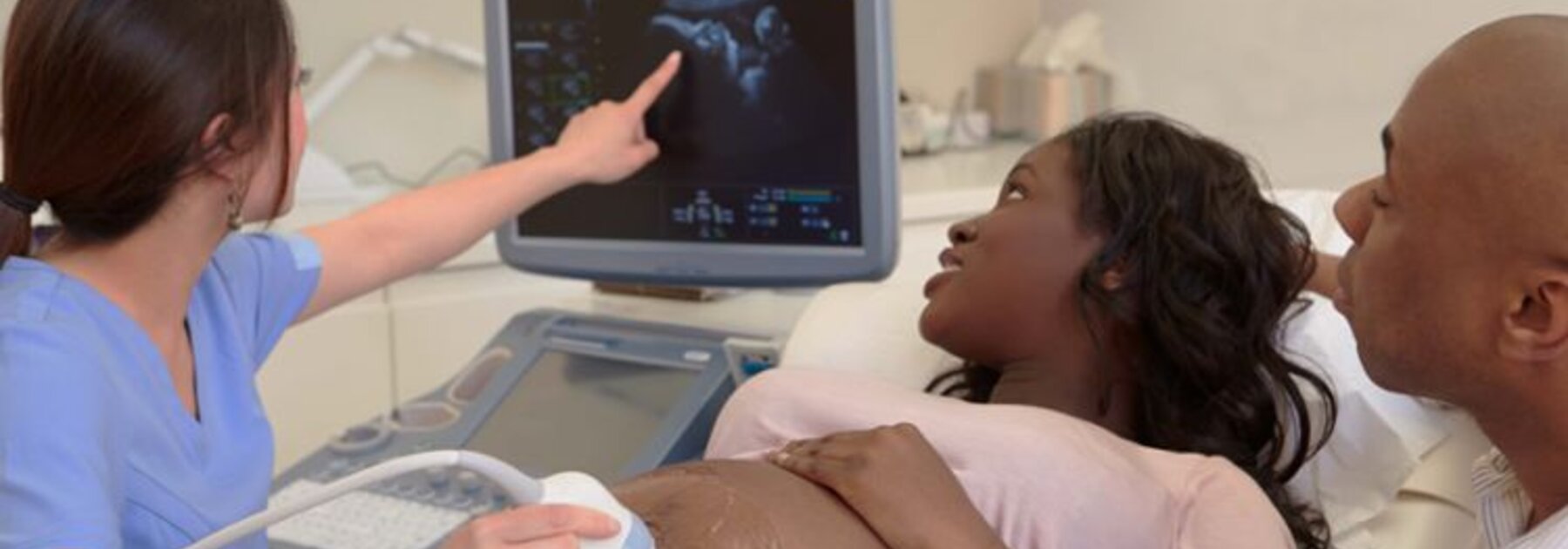 Een zwangere vrouw wordt onderzocht met een echografie terwijl de vader naast haar zit.