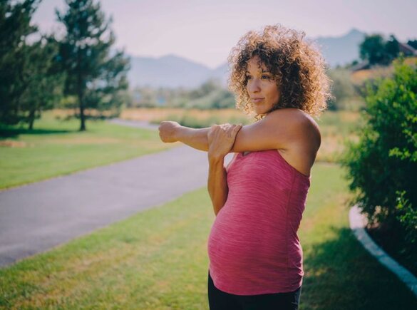 Een zwangere moeder die zich buiten uitrekt.