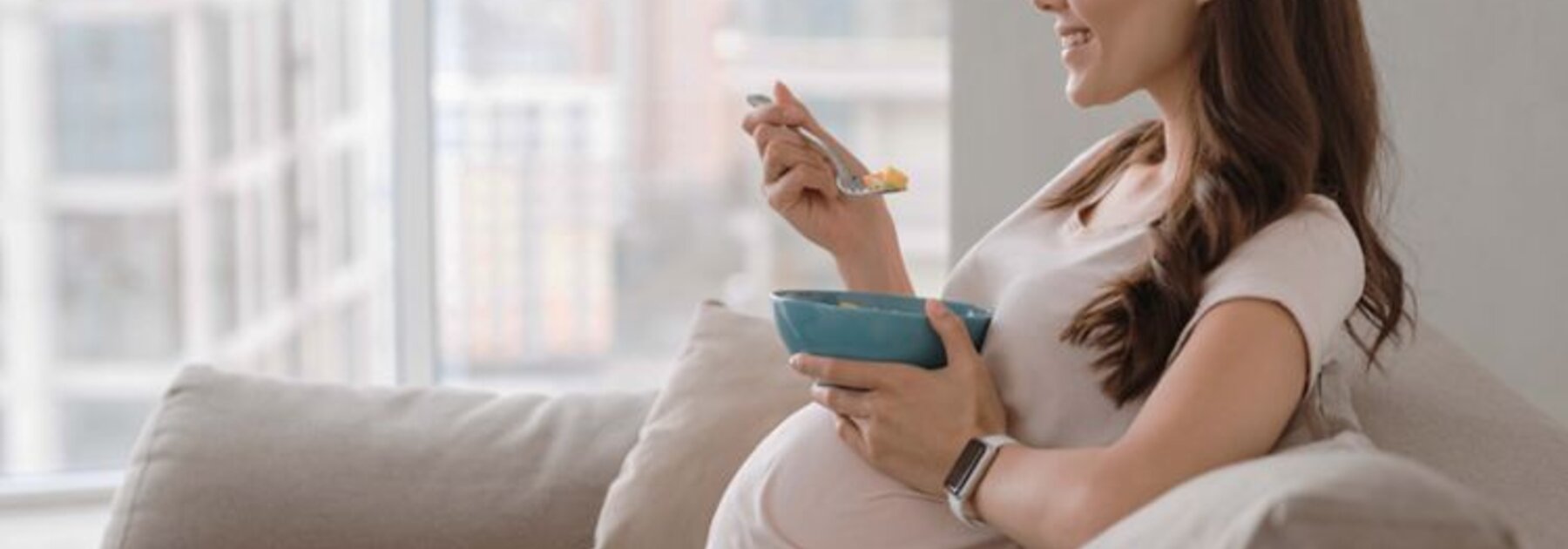 Zwangere moeder eet met haar benen gekruist en kijkt, terwijl ze op de bank zit.