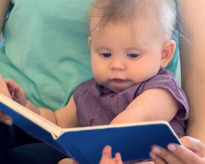 A mom and her baby read a book.