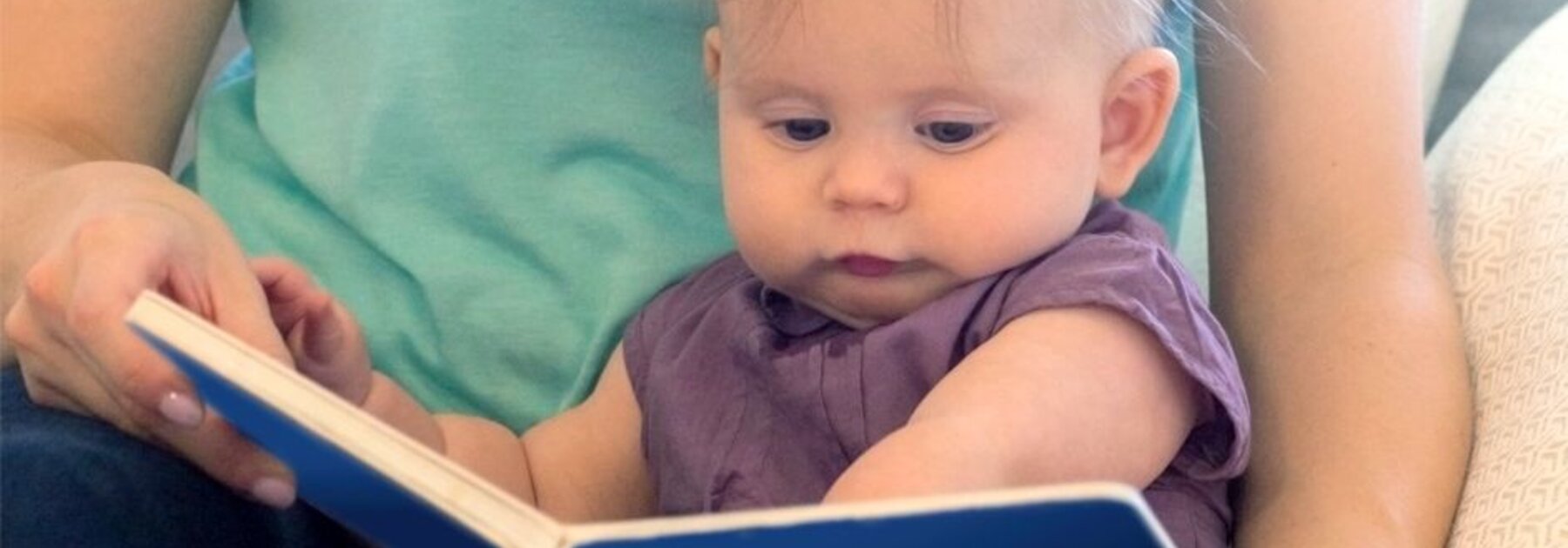 A mom and her baby read a book.