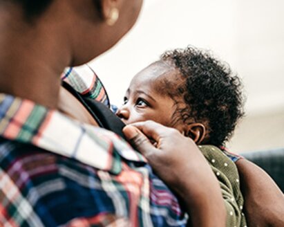 A mother breastfeeding her baby while it faces her.