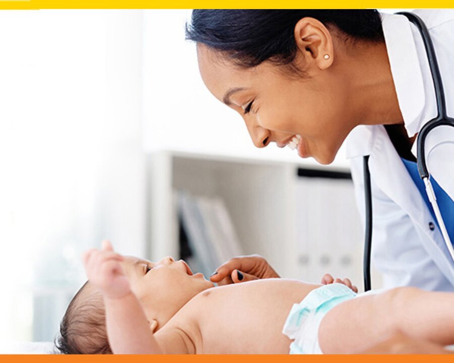 Baby on an exam table, medical professional leaning over baby smiling.