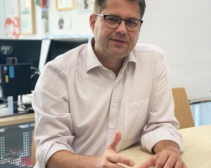 Keller Matthias sitting at a conference table with papers in front of him looking forward.