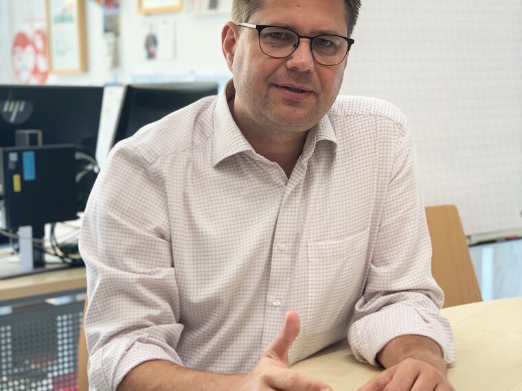 Keller Matthias sitting at a conference table with papers in front of him looking forward.