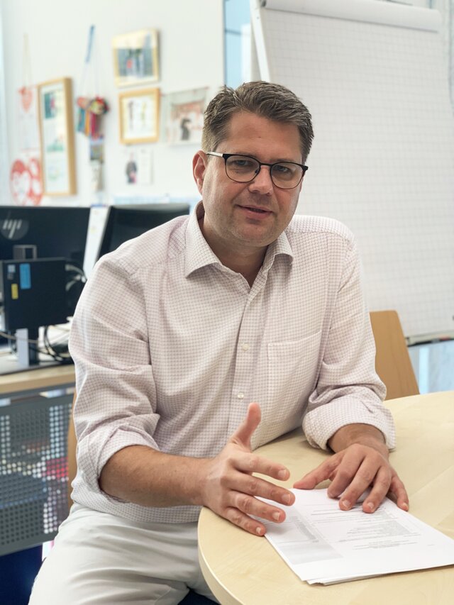 Keller Matthias sitting at a conference table with papers in front of him looking forward.