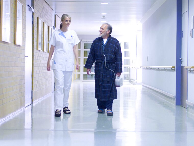 A doctor and a patient walk down a hospital corridor.