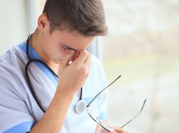 Eine Krankenschwester fühlt sich verbrannt und hält erschöpft den Kopf nach unten.