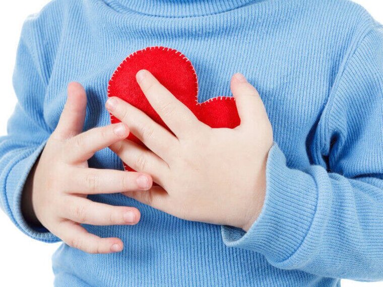 Ein Kind, das sich einer Kinderherzoperation unterziehen muss, hält ein Herz aus Stoff in der Hand.