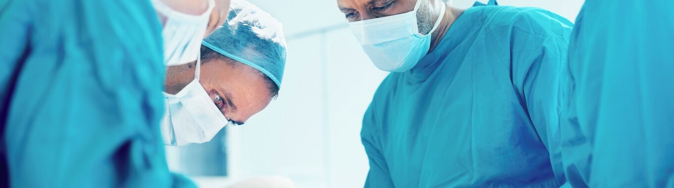 Surgical room with several doctors looking down on a patient.