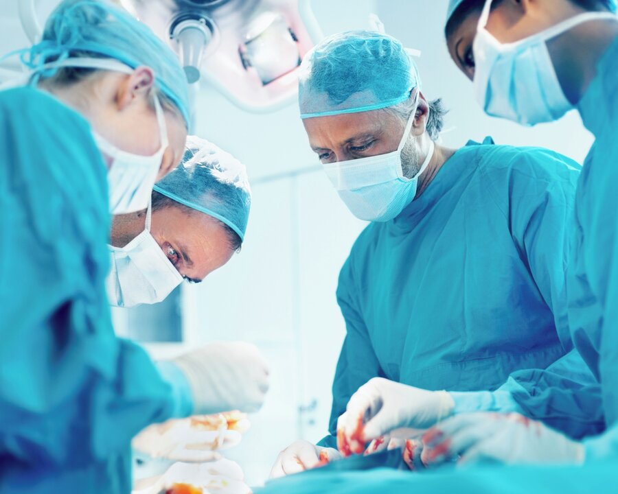Surgical room with several doctors looking down on a patient.