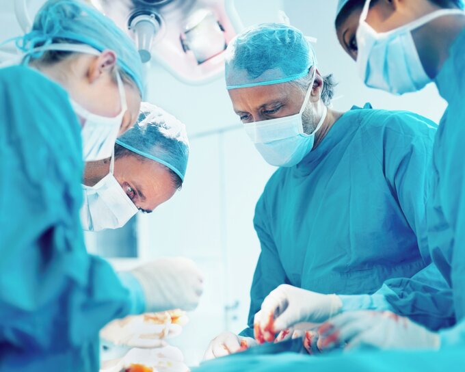Sala chirurgica con diversi medici che guardano un paziente.