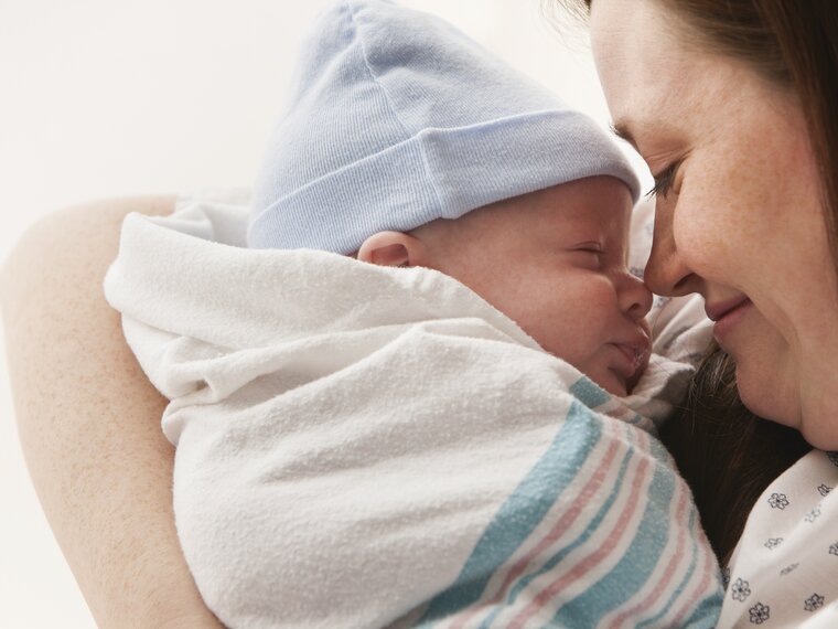 A mother holds her wrapped newborn baby close to her face in hospital.