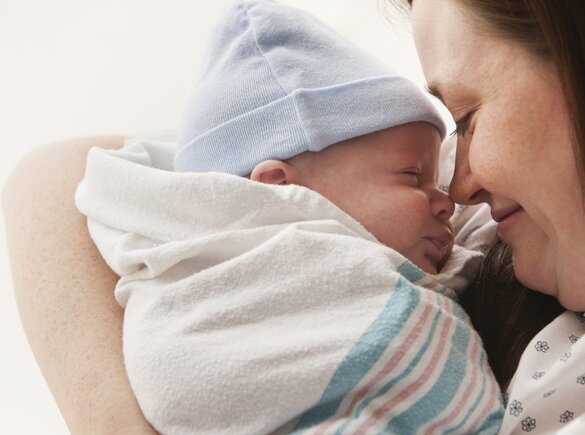 A mother holds her wrapped newborn baby close to her face in hospital.