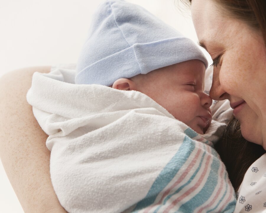 Pumping Tips A mother holds her wrapped newborn baby close to her face in hospital.