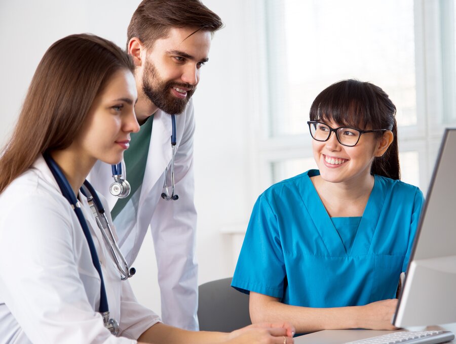 Eine Gruppe von drei medizinischen Fachkräften arbeitet zusammen und schaut auf einen Computerbildschirm.