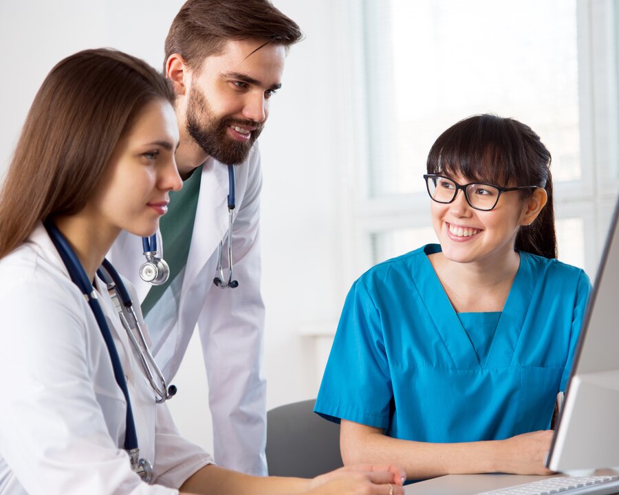 Group of three medical professionals working together and looking at a computer screen.