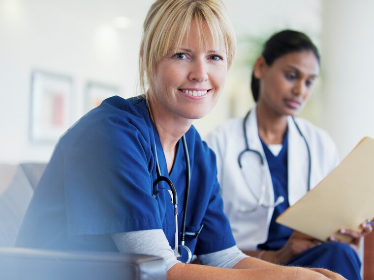 Ein Arzt lächelt in die Kamera, ein anderer Arzt sieht sich eine Akte an.