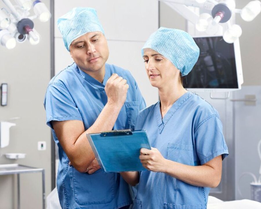 Zwei Mediziner, die in einem Operationssaal stehen und ein Krankenblatt betrachten.