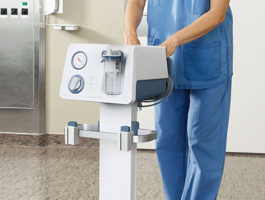 Salle d'opération montrant une infirmière poussant une pompe d'aspiration Medela Dominant