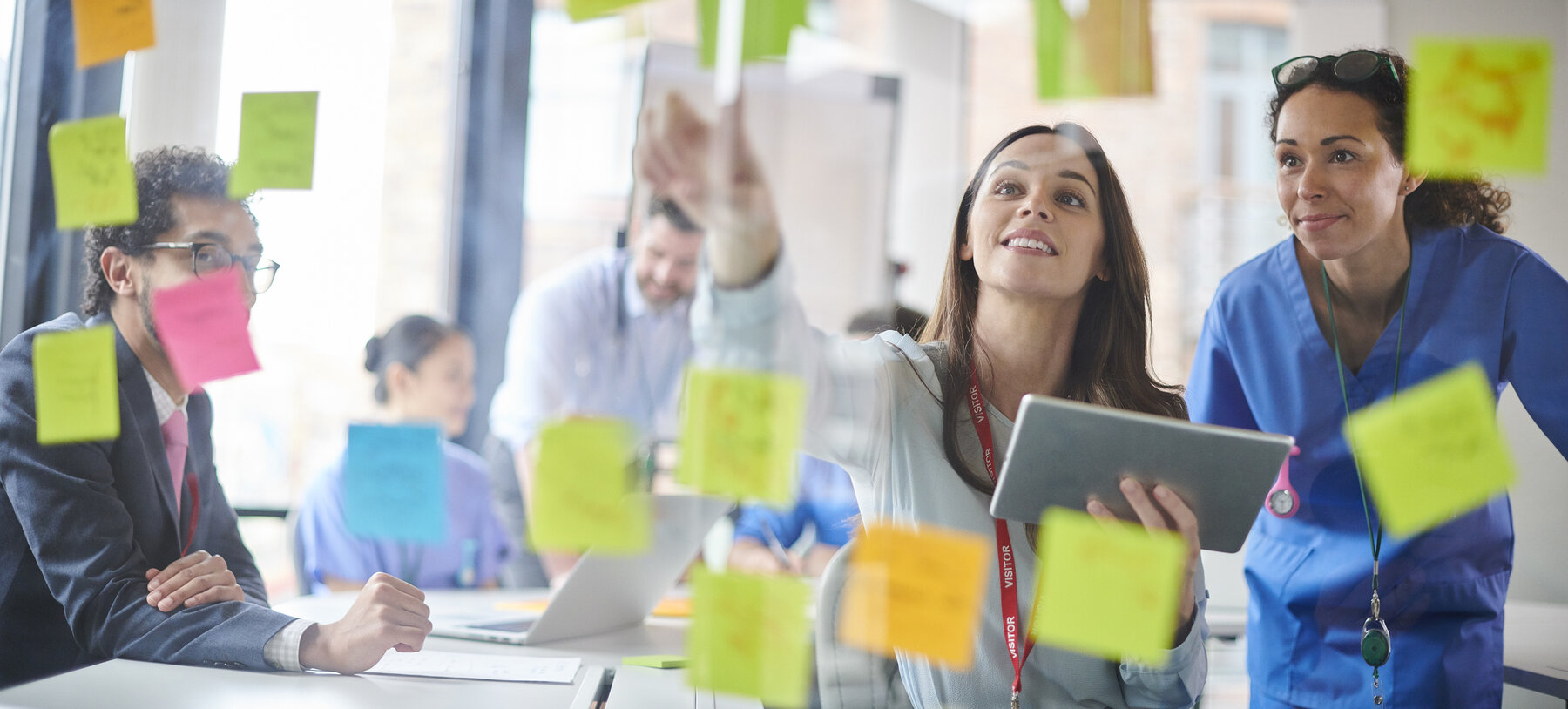 Looking through a window with notes stuck to it and you see a group of colleagues in a conference room working together