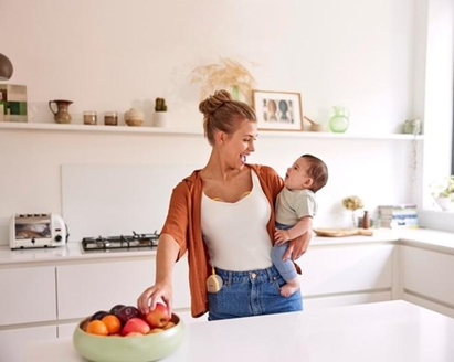 Una mamma tiene in braccio il suo bambino e fa uno spuntino mentre indossa il suo tiralatte elettrico doppio a mani libere Medela Freestyle™.e