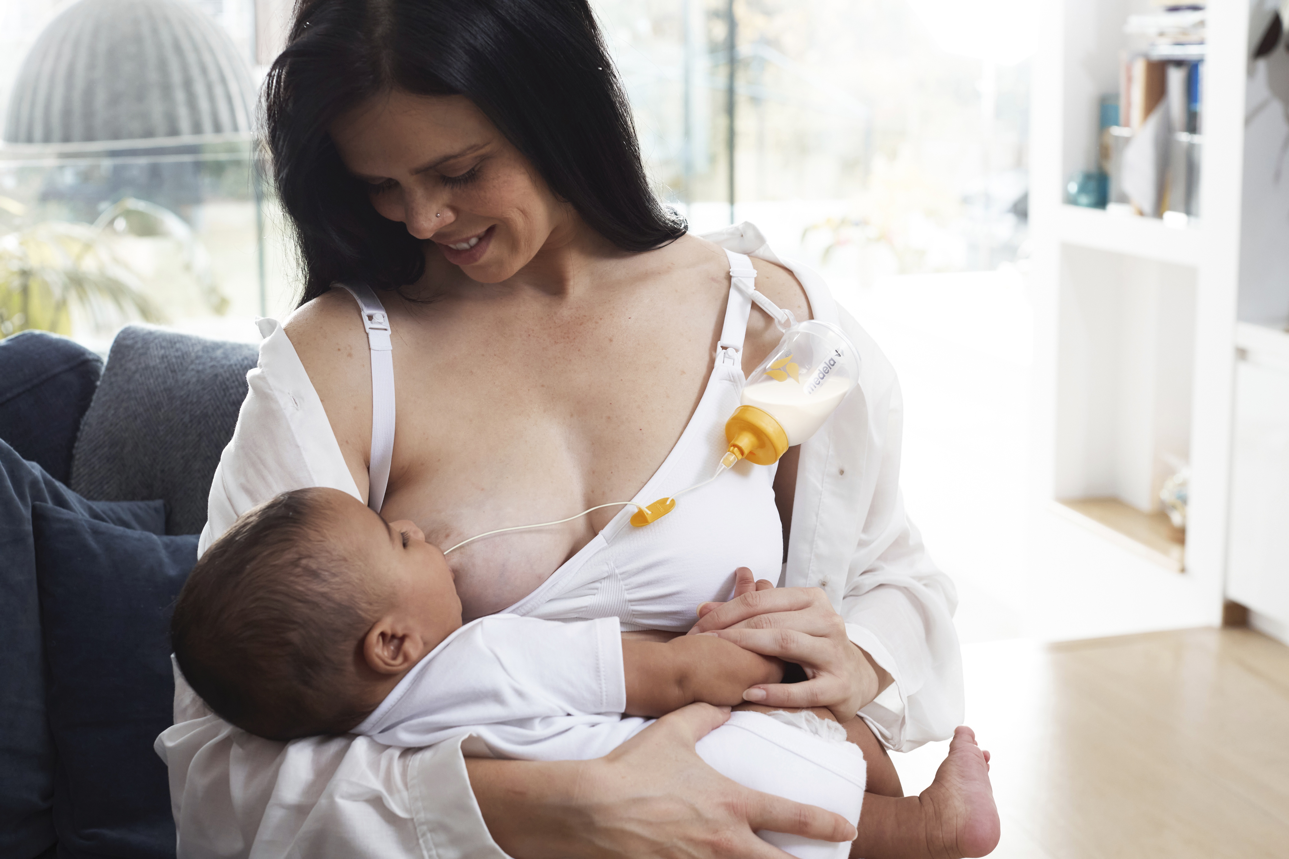 A mom breastfeeding her baby and supplementing the diet using Medela's Supplemental Nursing System™ (SNS).