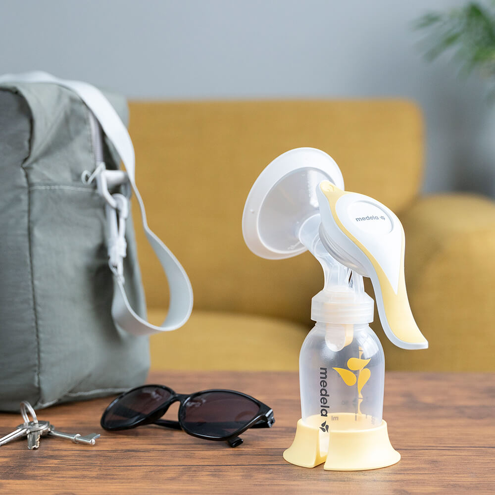 The Medela Harmony™ manual breast pump on a table at home ready to go with keys, glasses and diaper bag.
