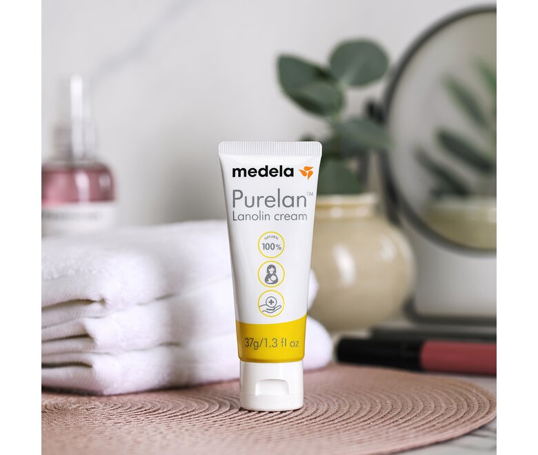 Medela Purelan™ Lanolincreme auf einem Badezimmertisch neben einer Pflanze und Handtüchern.
