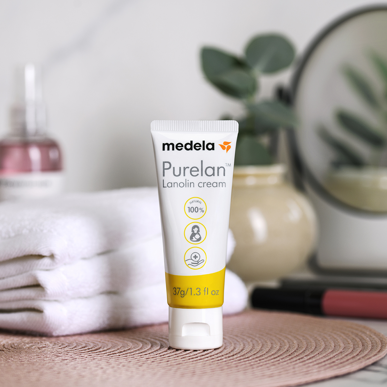 Medela Purelan™ Lanolincreme auf einem Badezimmertisch neben einer Pflanze und Handtüchern.