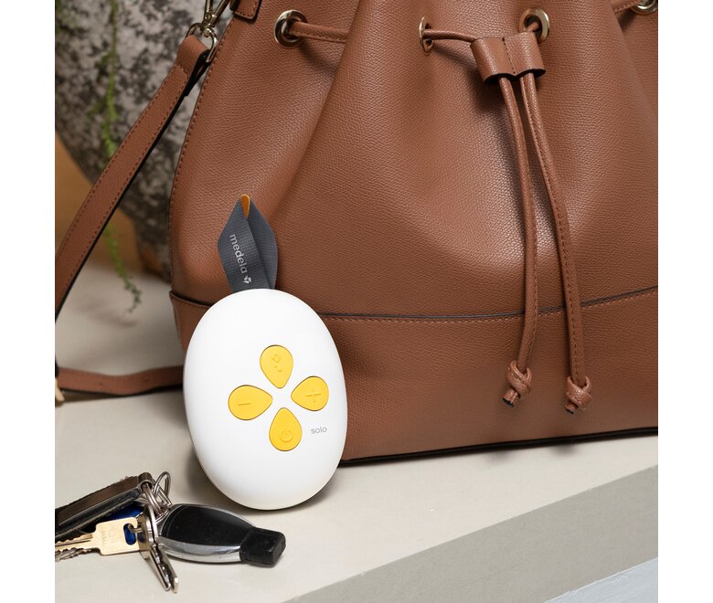 Il tiralatte elettrico singolo a mani libere Medela Solo™ sul bancone, vicino alla borsa e alle chiavi della mamma.