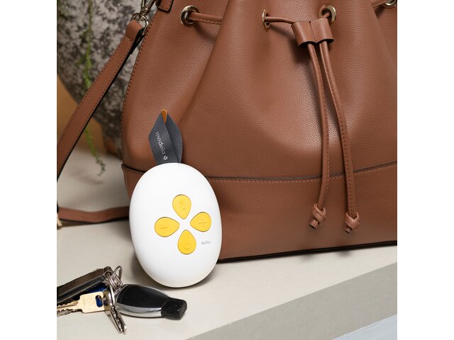 The Medela Solo™ Hands-free single electric breast pump on counter by mom's purse and keys.