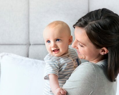 Uma mãe segura o seu bebé enquanto ambos sorriem.