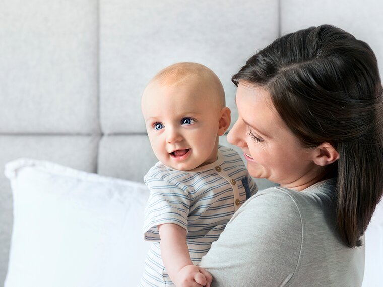 Une maman tient son bébé dans ses bras et tous deux sourient.