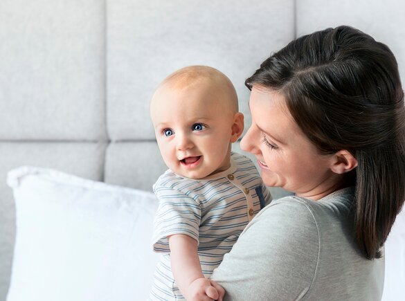 Uma mãe segura o seu bebé enquanto ambos sorriem.