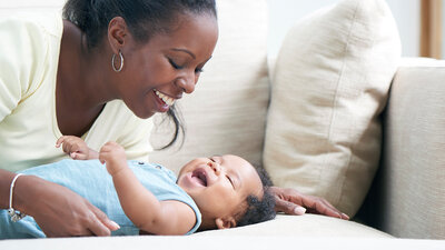 A mom plays with her baby on a couch.
