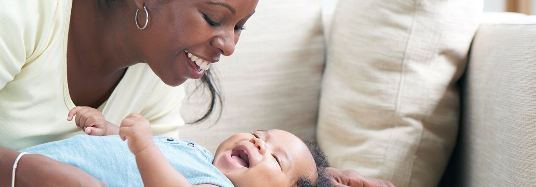 Uma mãe brinca com o seu bebé num sofá.